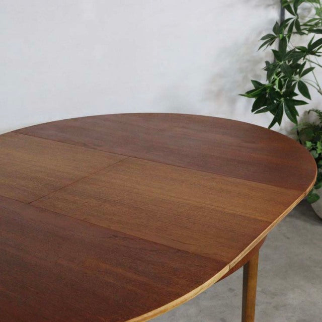 Round vintage teak dining table with smooth wood grain, British mid-century design, slender tapered legs.