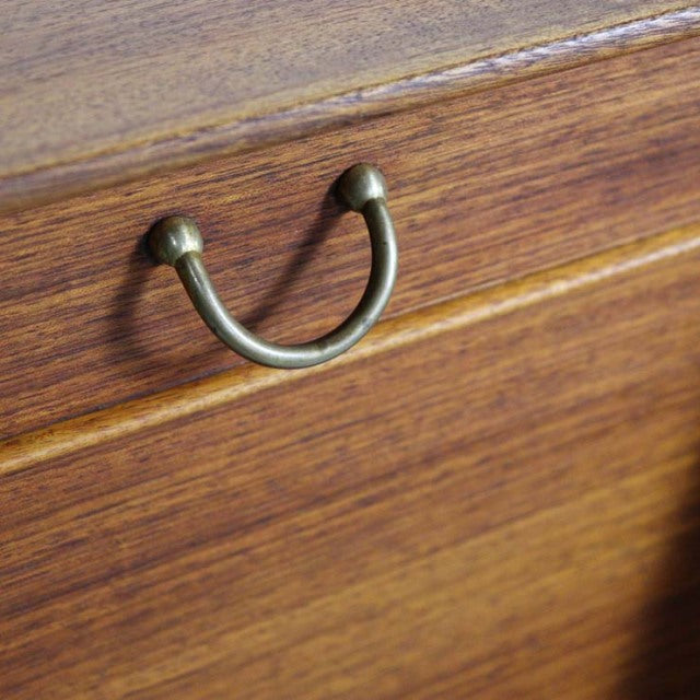 Close-up of vintage British G-Plan teak highboard drawer with mid-century brass curved handle and rich wood grain.