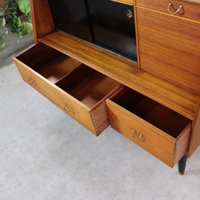 Mid-century British G-Plan teak highboard with rich wood grain, brass handles, black sliding doors, and tapered legs.