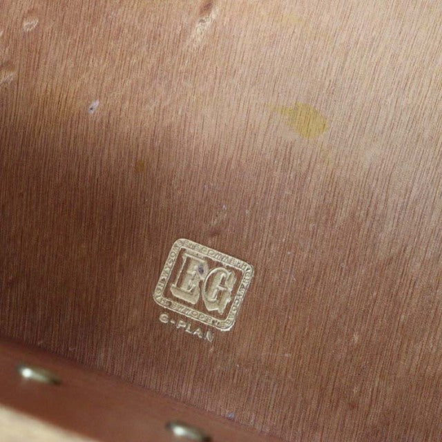 Close-up of vintage G-PLAN gold stamp logo on mid-century British teak wood with visible grain texture and natural finish.