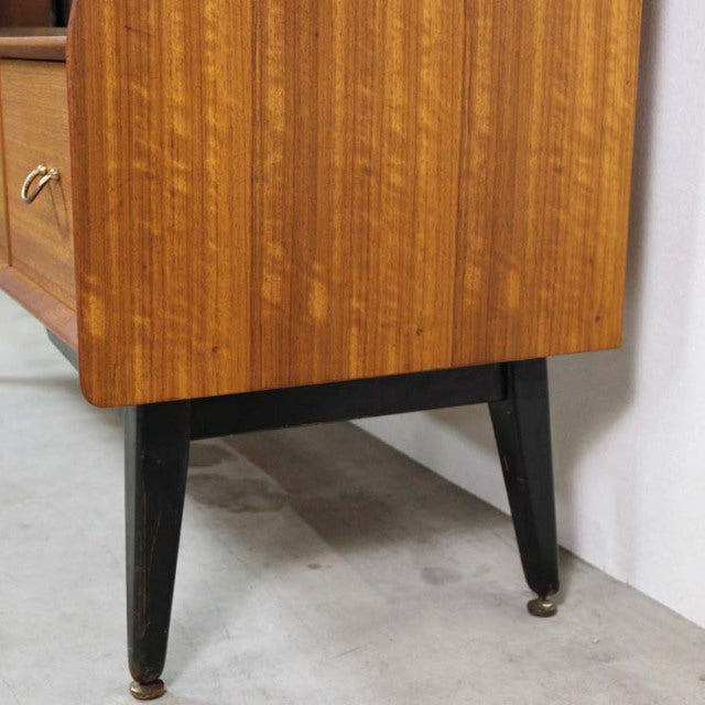 Vintage mid-century British teak sideboard corner with rich wood grain and tapered black legs with brass feet.