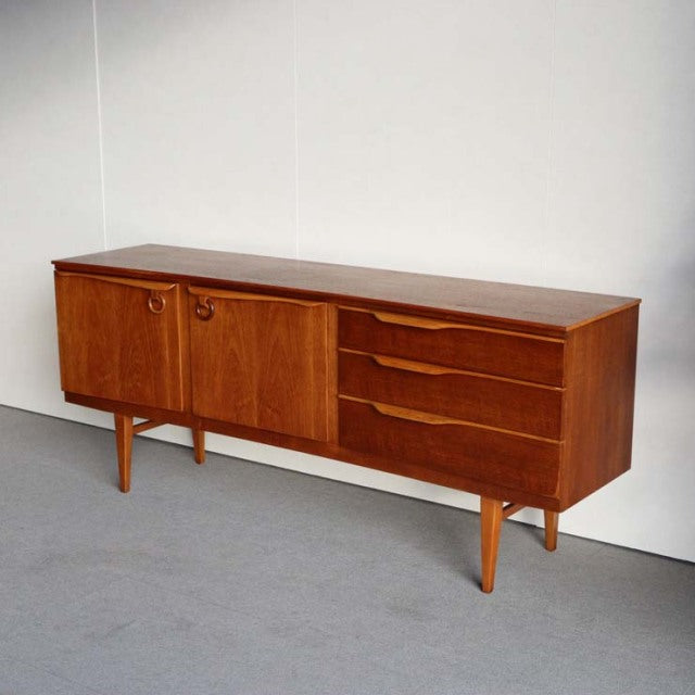 Vintage British mid-century teak sideboard by Beautility with smooth wood grain, tapered legs, two doors, and three drawers.