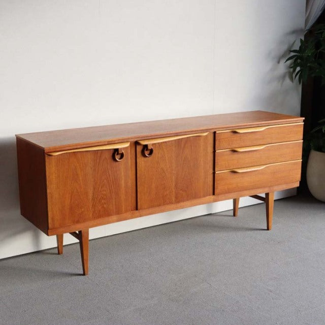 Mid-century British teak sideboard by Beautility with rich wood grain, curved drawer handles, rounded cabinet doors, and.