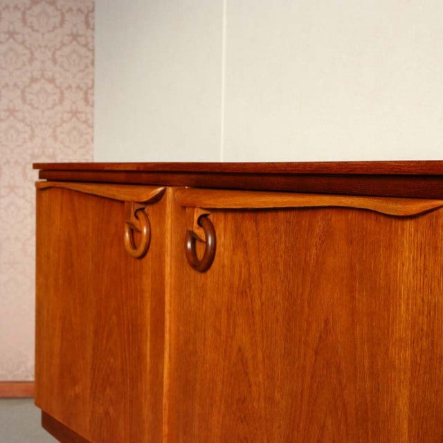 Vintage mid-century teak sideboard by Beautility featuring smooth wood grain, curved handles, and slender tapered legs in.