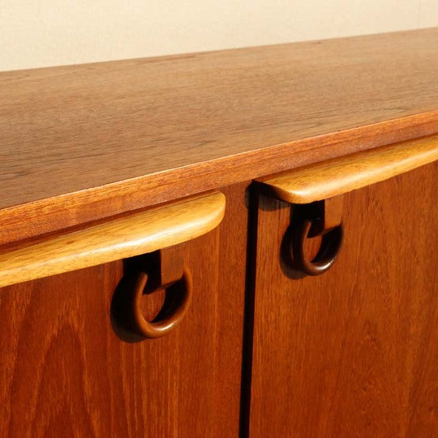 Vintage mid-century teak sideboard with smooth wood grain and distinctive curved handles, British-Danish design.