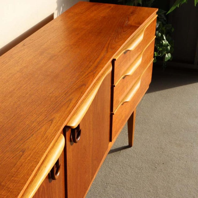 Vintage teak sideboard by Beautility with mid-century British and Danish design, sleek wood grain, elegant tapered legs, and .