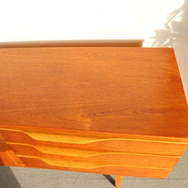 Mid-century British teak sideboard by Beautility with smooth wood grain, sculpted drawer fronts, and tapered legs in warm.