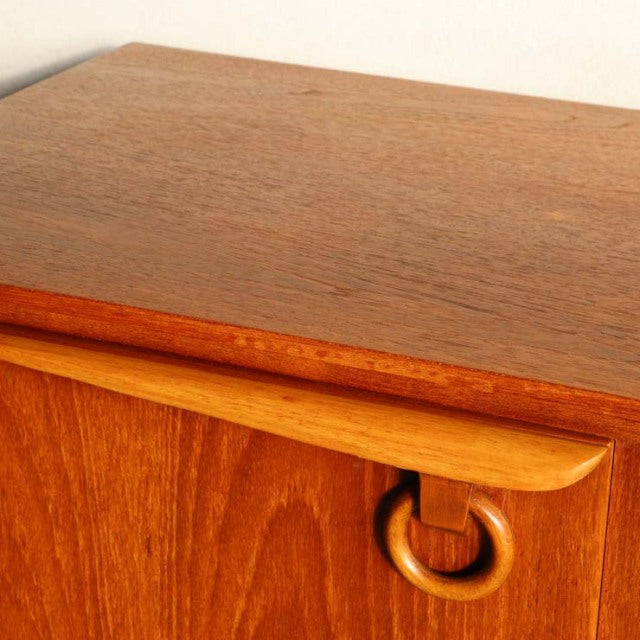 Vintage teak sideboard by Beautility featuring smooth wood grain, rounded edges, and distinctive circular wooden handle,.
