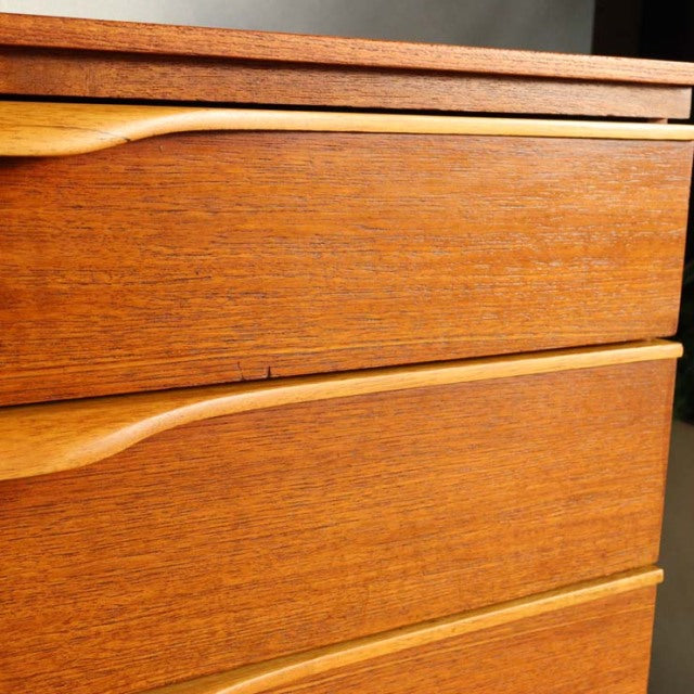 Close-up of vintage teak sideboard drawer fronts showcasing smooth wood grain and curved British mid-century handles,.