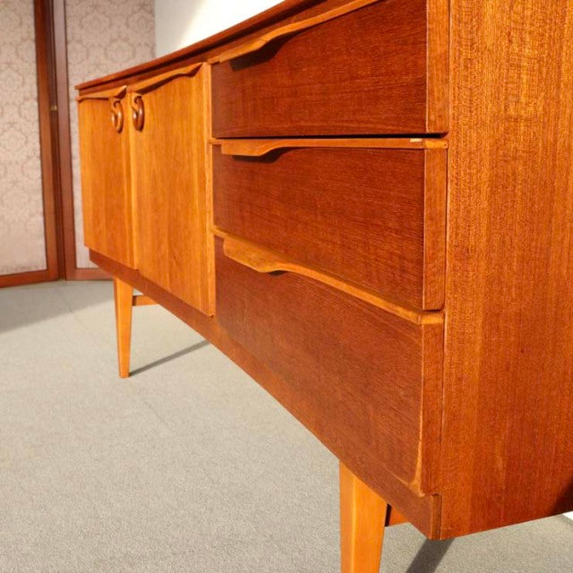 Mid-century British teak sideboard by Beautility with smooth wood grain, tapered legs, and curved drawer handles in vintage.