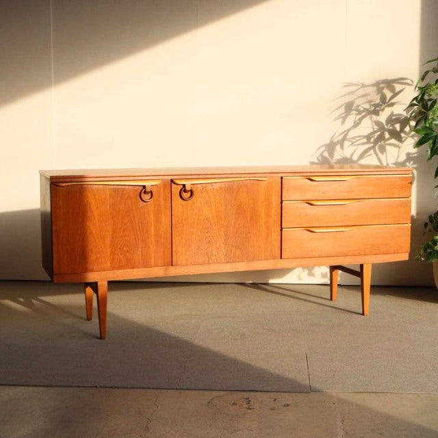 Mid-century British teak sideboard by Beautility with rich wood grain, elegant tapered legs, two doors with circular metal.