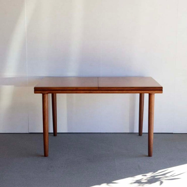 Mid-century British teak dining table by WhiteANDnewton with rectangular top, slender tapered legs, smooth wood grain finish.