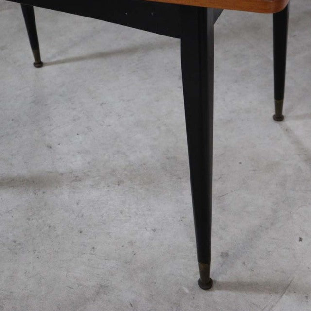 Vintage mid-century teak dining table with sleek black tapered legs and brass-capped feet, showcasing rich wood grain and.