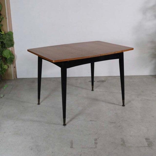 Mid-century vintage British teak dining table with rectangular top, slender black tapered legs, and brass-tipped feet.