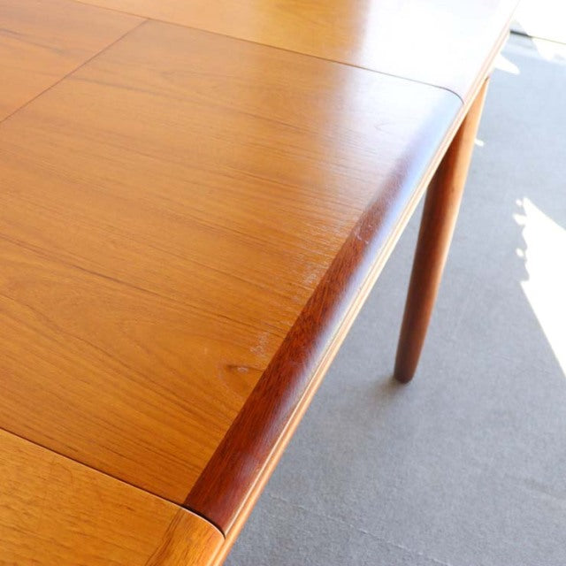 Vintage British mid-century teak dining table with rectangular top and tapered legs, showcasing rich wood grain and warm.