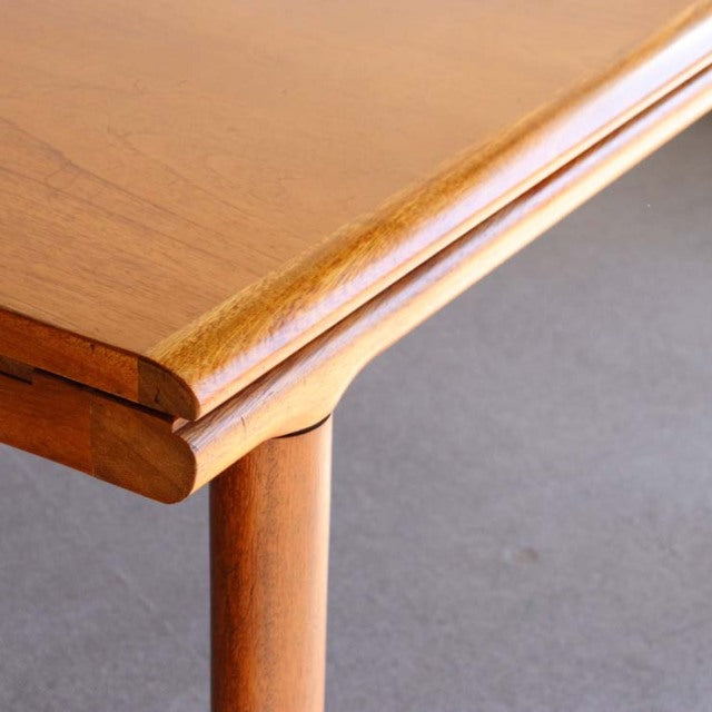 Vintage teak dining table corner with smooth wood grain, rounded edge, and slender British mid-century Denmark-style leg.