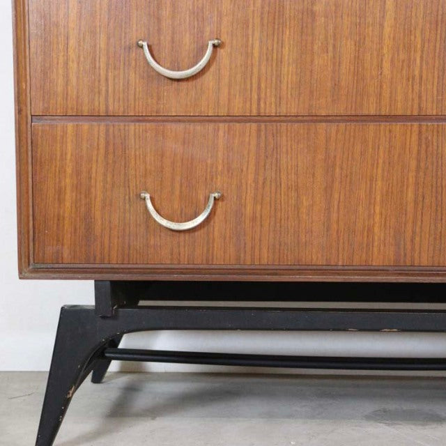 Mid-century British vintage teak chest with rich wood grain, curved metal handles, and black tapered legs from Meredew,.