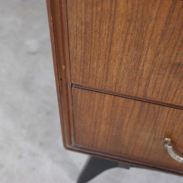 Vintage mid-century teak chest corner with visible wood grain and brass handle on black tapered legs.