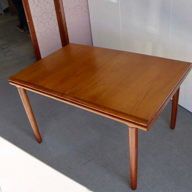 Vintage British mid-century teak dining table with smooth wood grain and tapered rounded legs, rectangular design.