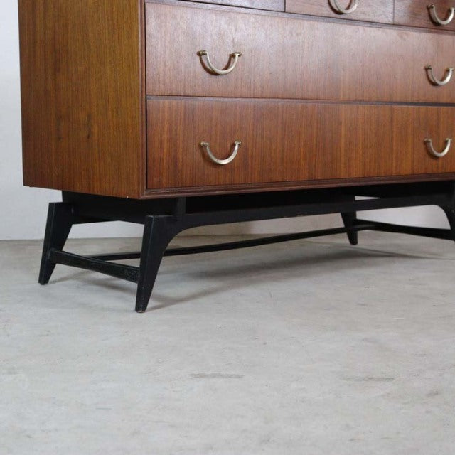 Mid-century British teak chest with rich wood grain, curved brass handles, and black tapered legs from Meredew.