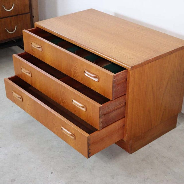 Vintage British G-Plan mid-century teak chest with three open drawers, smooth wood grain, tapered legs, and clean.