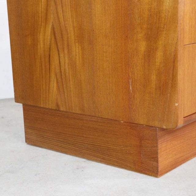 Close-up of British vintage G-plan teak wood mid-century chest corner with natural wood grain and raised base.
