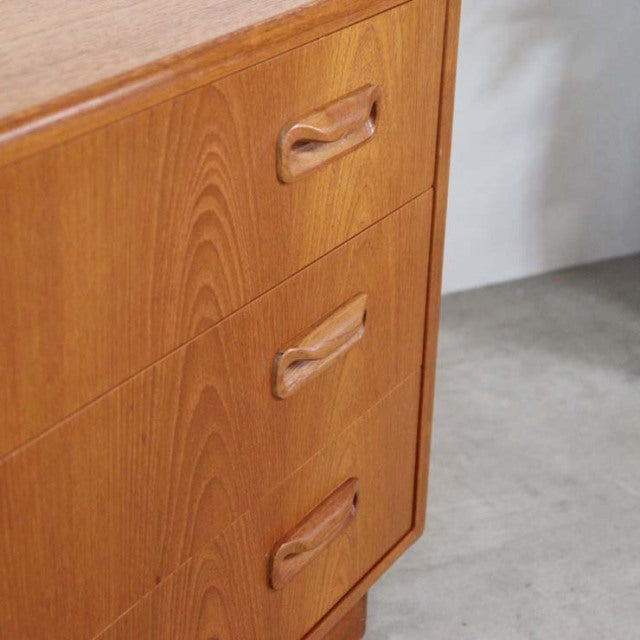 Vintage G-Plan teak three-drawer chest with warm wood grain, sculpted recessed handles, and tapered mid-century British legs.