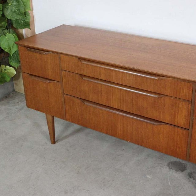 Mid-century vintage British teak sideboard with smooth wood grain, tapered legs, and rounded drawer handles from Denmark.