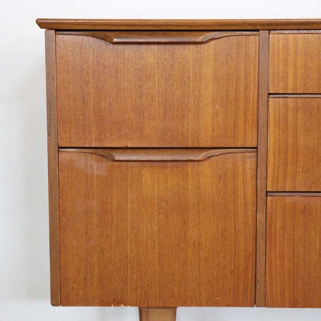 Vintage British mid-century teak sideboard segment with smooth wood grain and curved drawer handles, showcasing clean lines.