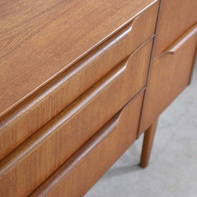 Vintage teak British mid-century sideboard with smooth wood grain, recessed drawer handles, and tapered legs from Denmark.