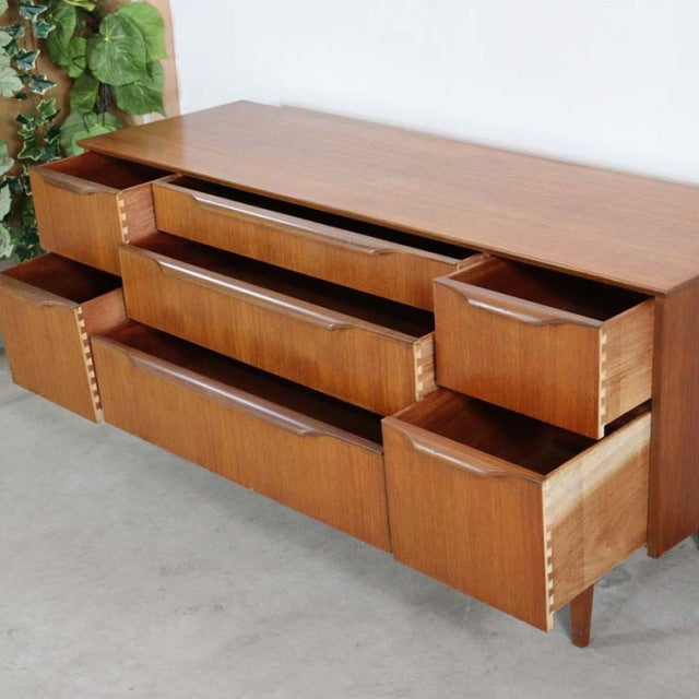 Mid-century British teak sideboard with five drawers, clean lines, visible wood grain, and tapered legs.
