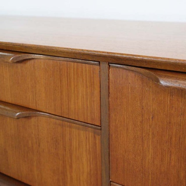 Mid-century British vintage teak sideboard with smooth wood grain and integrated curved handles.