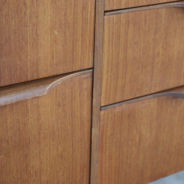 Close-up of vintage British teak sideboard drawer fronts showcasing smooth grain and curved recessed handles, mid-century.