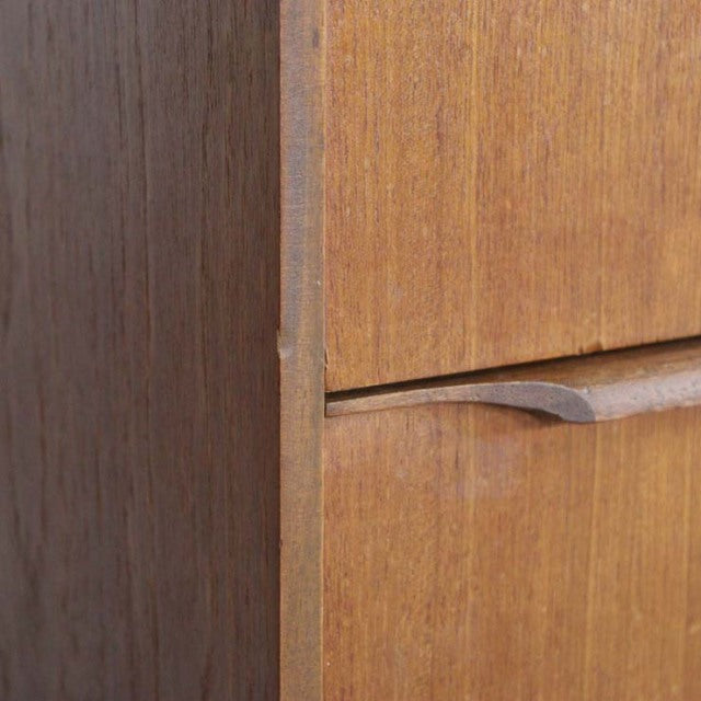 Mid-century British vintage teak sideboard corner showing smooth wood grain and curved drawer handle detail.
