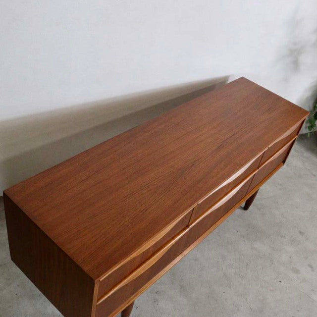 Vintage British mid-century teak sideboard with sleek grain, smooth surface, and tapered legs from Austinsuite.