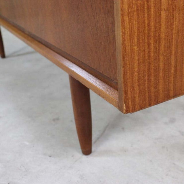Close-up of mid-century British vintage Austinsuite teak sideboard leg with warm wood grain and tapered cylindrical design.