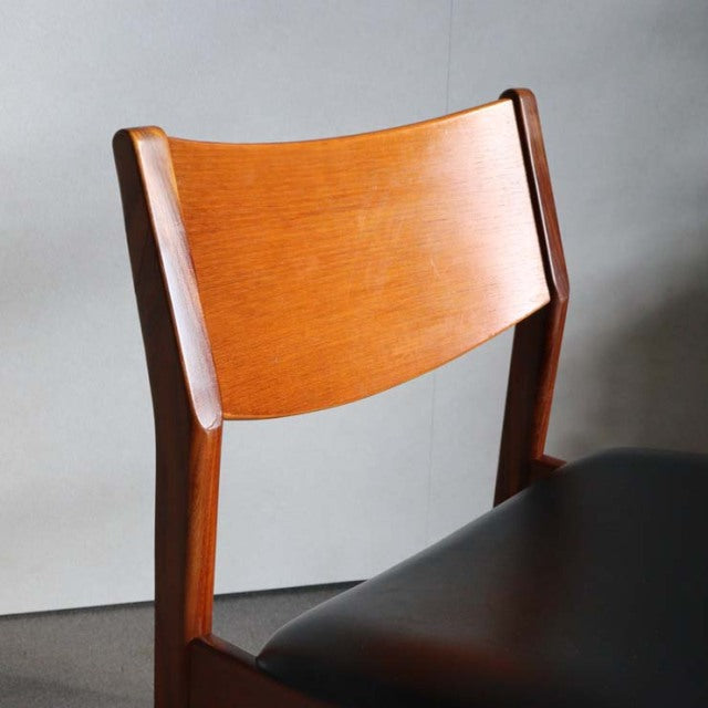 Mid-century British teak dining chair with curved backrest and dark leather seat cushion, vintage craftsmanship visible in.