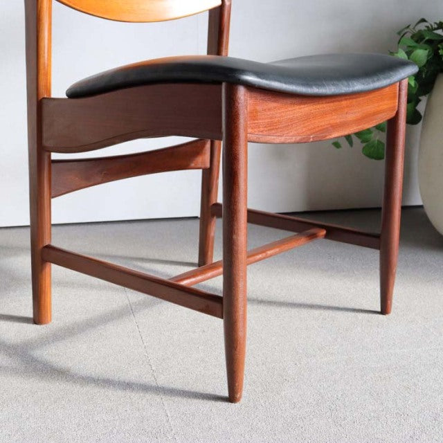 Mid-century British vintage teak dining chair with curved backrest and black cushioned seat, sleek tapered legs.