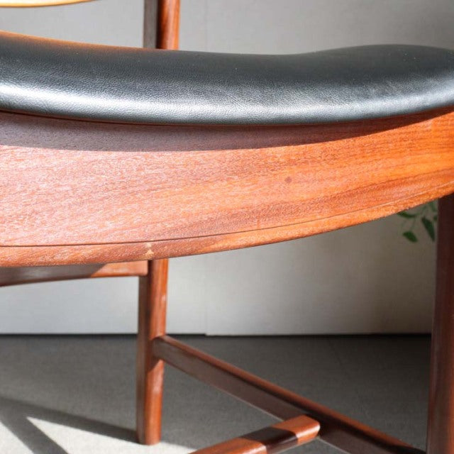 Close-up of vintage British mid-century teak chair showing smooth wood grain and black leather cushioned seat edge.