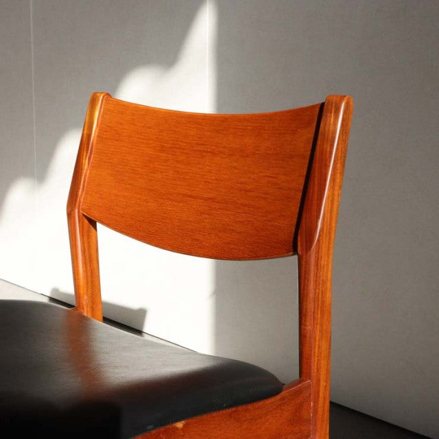 Mid-century British vintage teak dining chair with gently curved backrest and black leather seat cushion, showcasing warm.