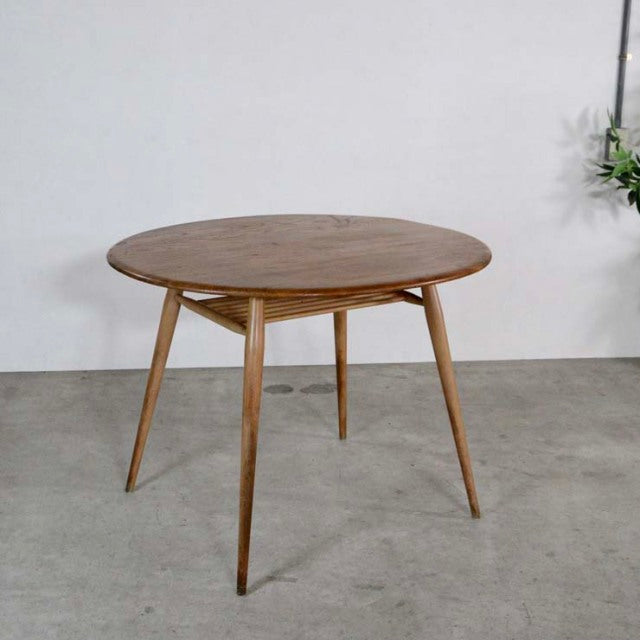 Vintage British mid-century ERCOL teak round dining table with smooth wood grain and tapered legs.