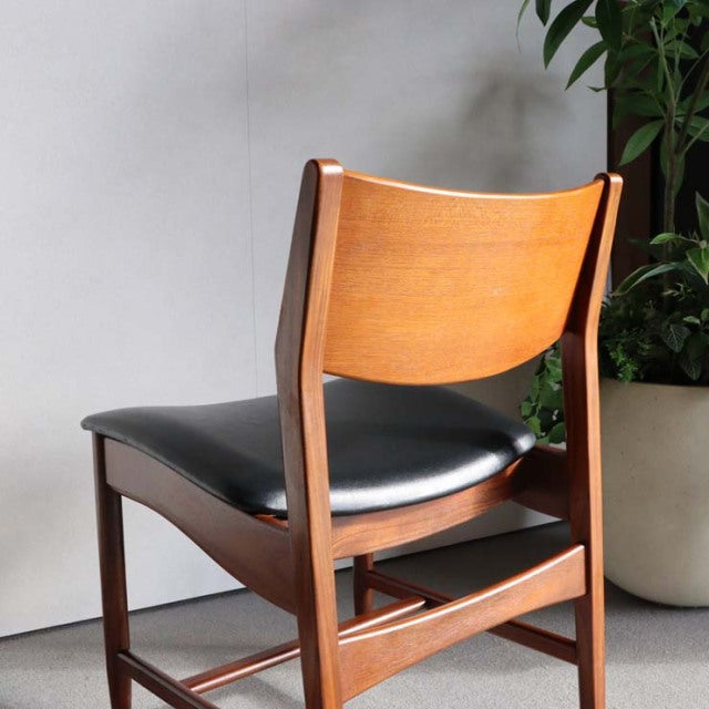 Vintage British mid-century dining chair in teak with black leather seat, sleek angled legs, and curved backrest showing.