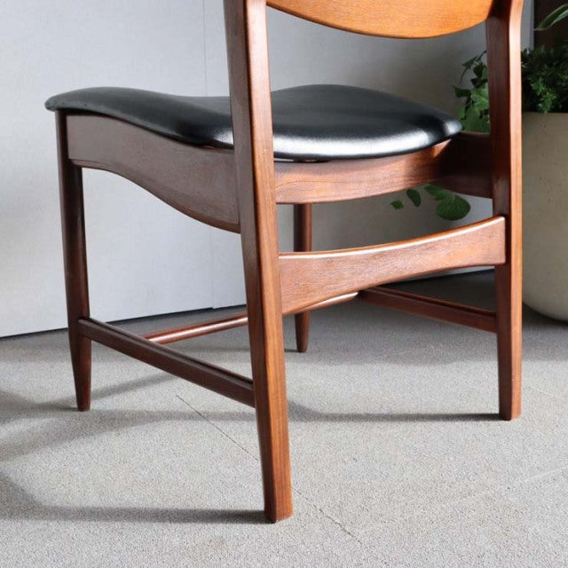 Vintage British mid-century teak dining chair with sleek wood grain and black leather seat cushion.