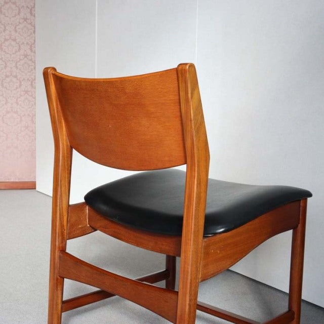 Mid-century British vintage teak dining chair with black leather seat, curved backrest, and tapered legs.
