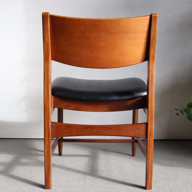 Mid-century British vintage teak dining chair with curved backrest and black leather seat cushion.