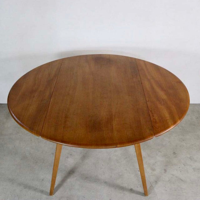 Vintage British mid-century Ercol dining table in teak with round drop-leaf top and slender tapered legs.