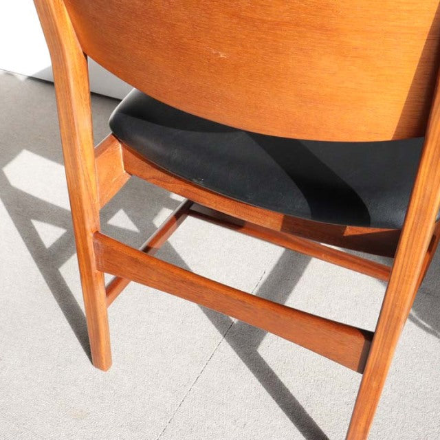 Mid-century British vintage teak dining chair with sleek black seat and curved backrest, showing rich wood grain and sturdy.