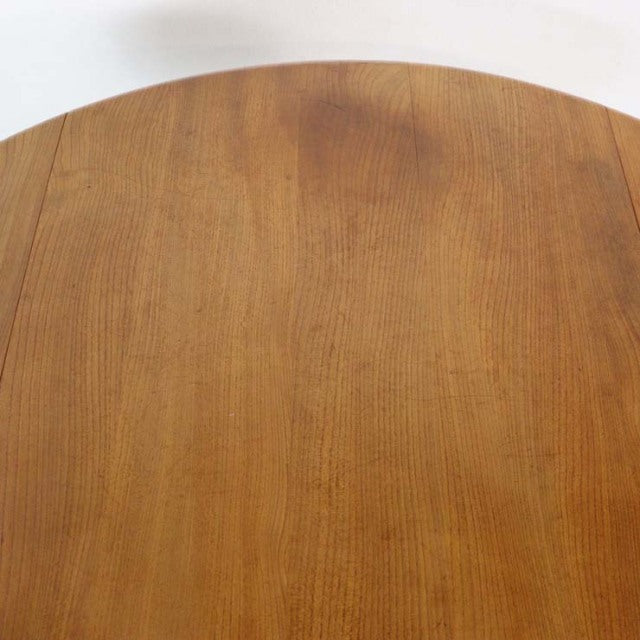 Vintage British mid-century Ercol dining table in warm teak with smooth round drop-leaf top and slender tapered legs.