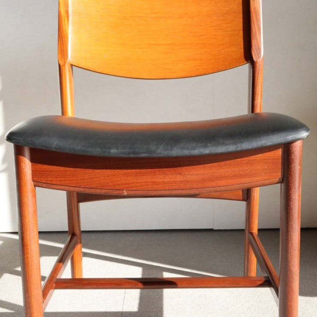 Mid-century British vintage teak dining chair with curved backrest and black leather seat cushion, sleek tapered legs.