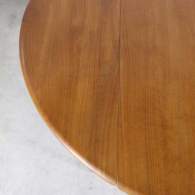 Vintage British Ercol mid-century teak dining table with drop-leaf, smooth wood grain, rounded edge.
